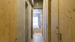 A corridor with wooden walls and a concrete ceiling, leading to a room with a bed and a window. - Smi:re Stay Oshiage (Tokyo)