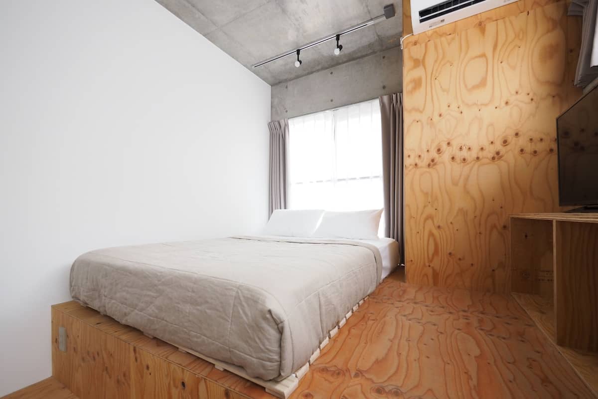 A bedroom with a bed on a wooden platform, a window with curtains, and a wooden wall.