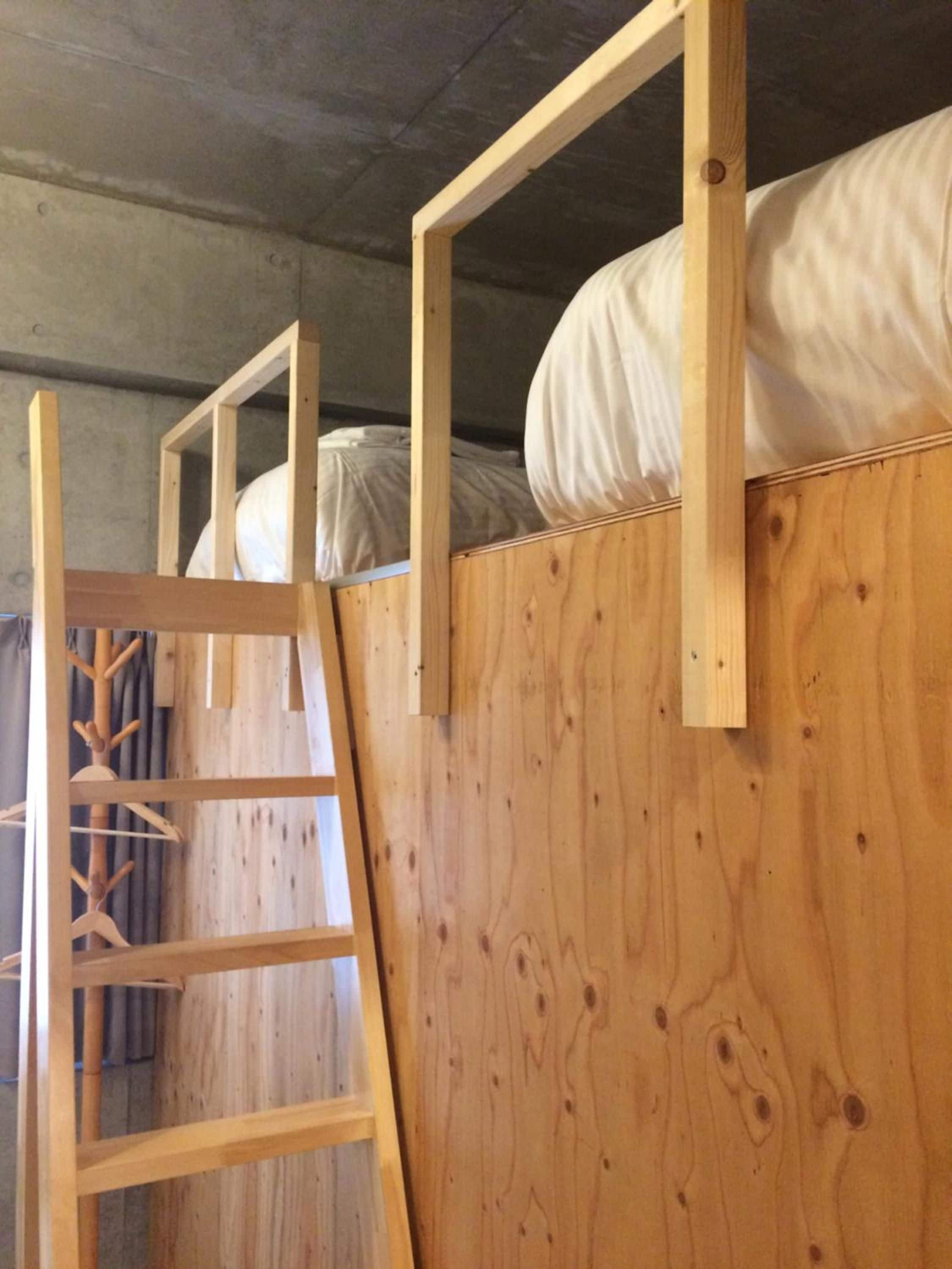 A wooden bunk bed with a ladder, a white mattress, and a wooden headboard.