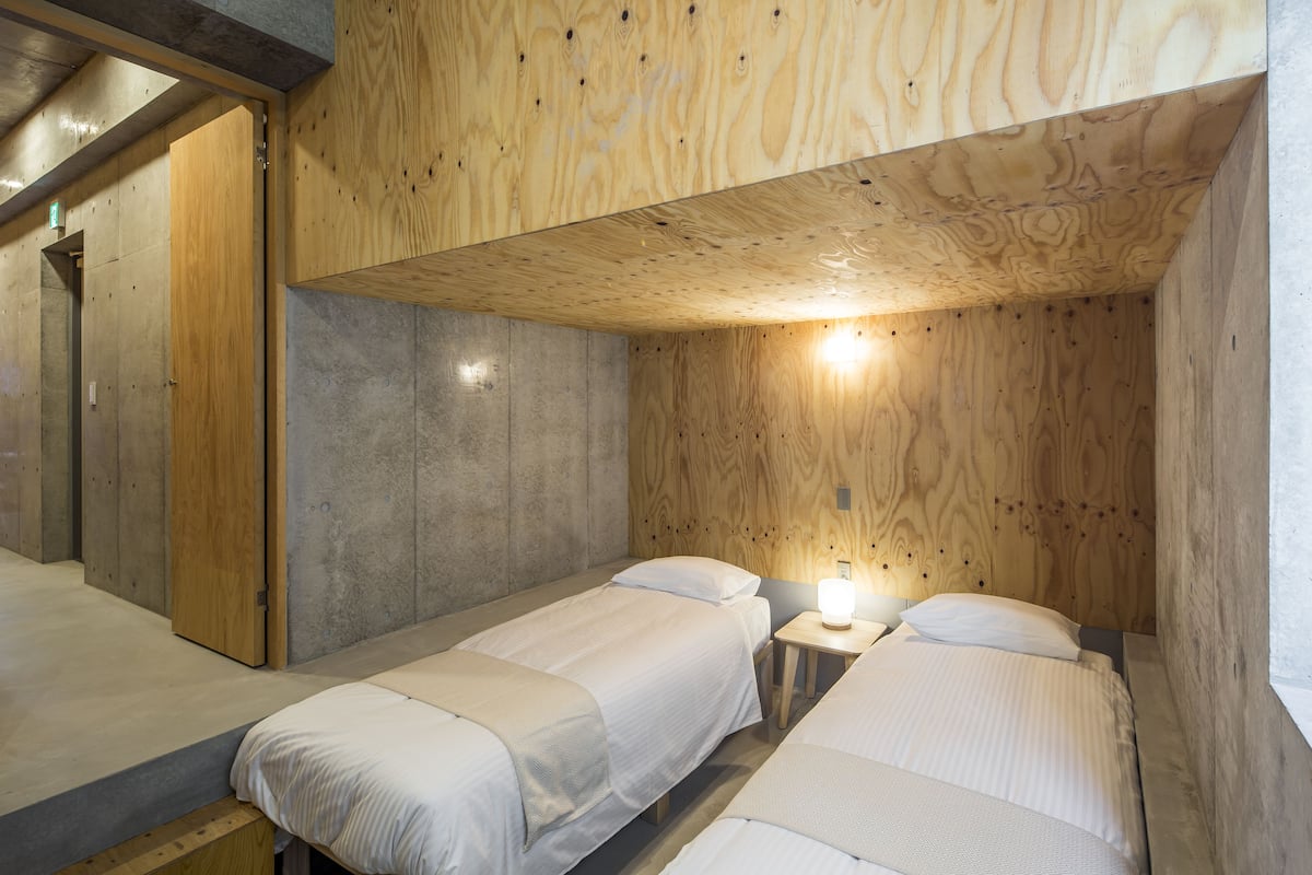 A room with two beds, wooden ceiling, and a small bedside table with a lamp.