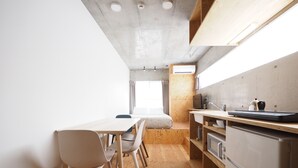 A compact kitchen with wooden cabinets, a dining area with chairs, and a built-in oven. - Smi:re Stay Oshiage (Tokyo)