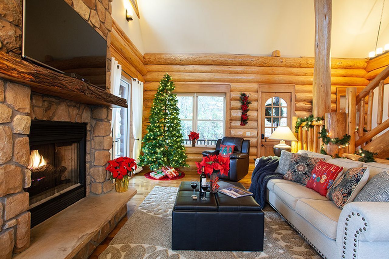 A cozy log cabin interior with a stone fireplace, a Christmas tree, and a comfortable seating area.