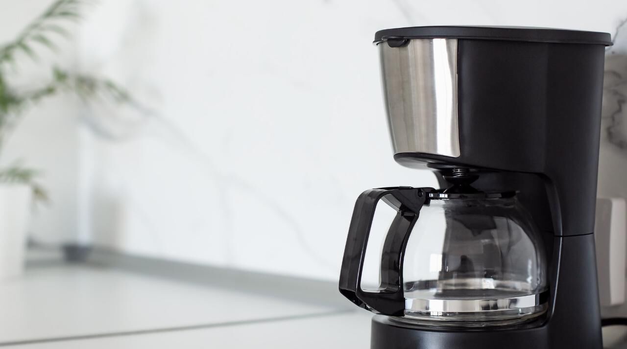 Una macchina per caffè espresso nera con serbatoio trasparente e vassoio raccogligocce metallico.