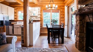 L’intérieur d’une cabane en rondins comprend un coin repas, une cuisine et une cheminée en pierre.