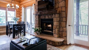 L’intérieur d’une cabane en rondins, avec une cheminée en pierre, un coin repas et un espace salon confortable.