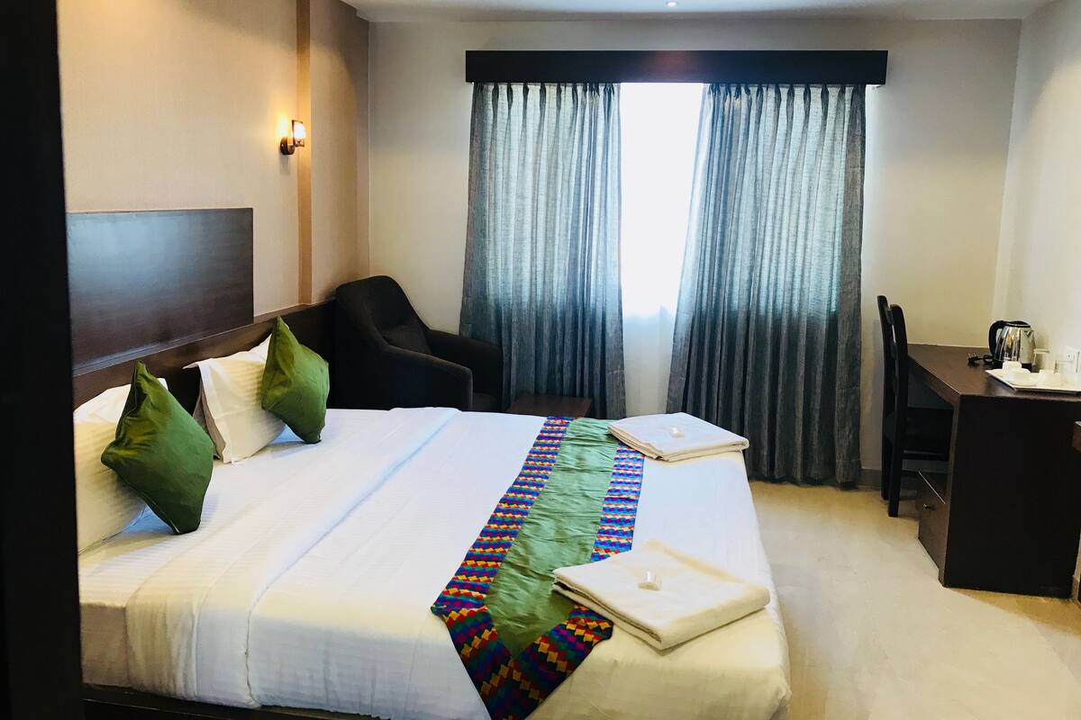 A hotel room with a bed, a desk, a chair, and a window with curtains.