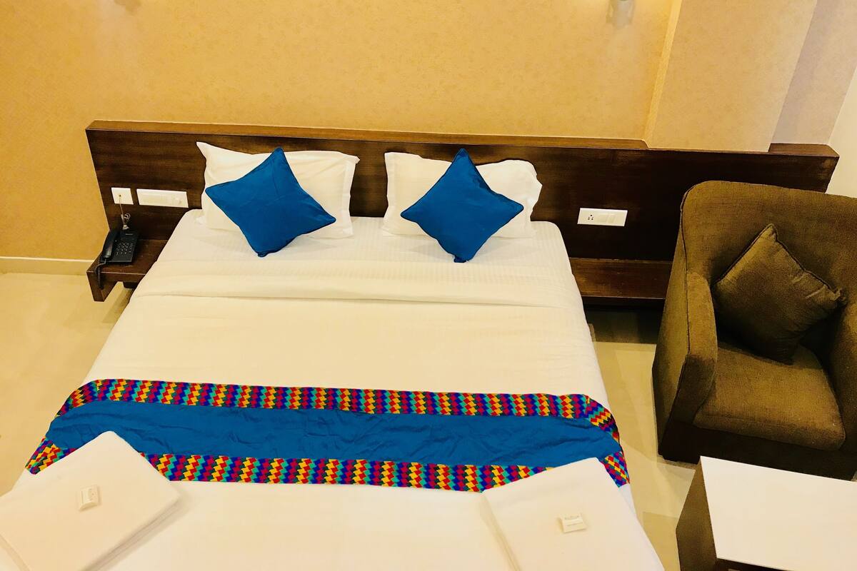 A hotel room with a bed, a chair, and a nightstand with a phone.