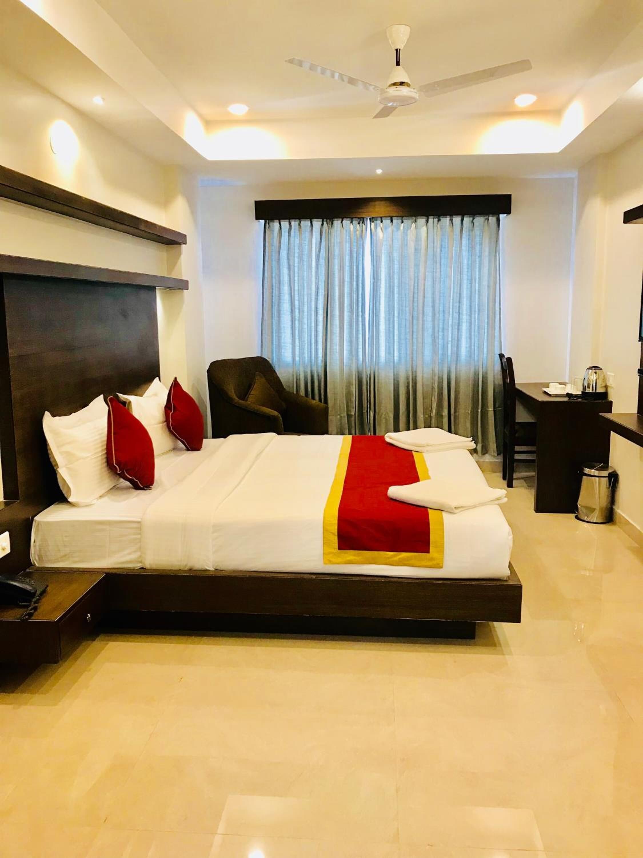 A hotel room with a bed, a desk, a chair, a ceiling fan, and a window with curtains.