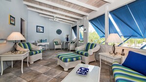Ein sonnendurchflutetes Zimmer mit Korbmöbeln, einem Deckenventilator und großen Fenstern.