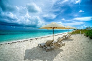 A beach with white sand, turquoise water, and a row of white lounge chairs under beige umbrellas.