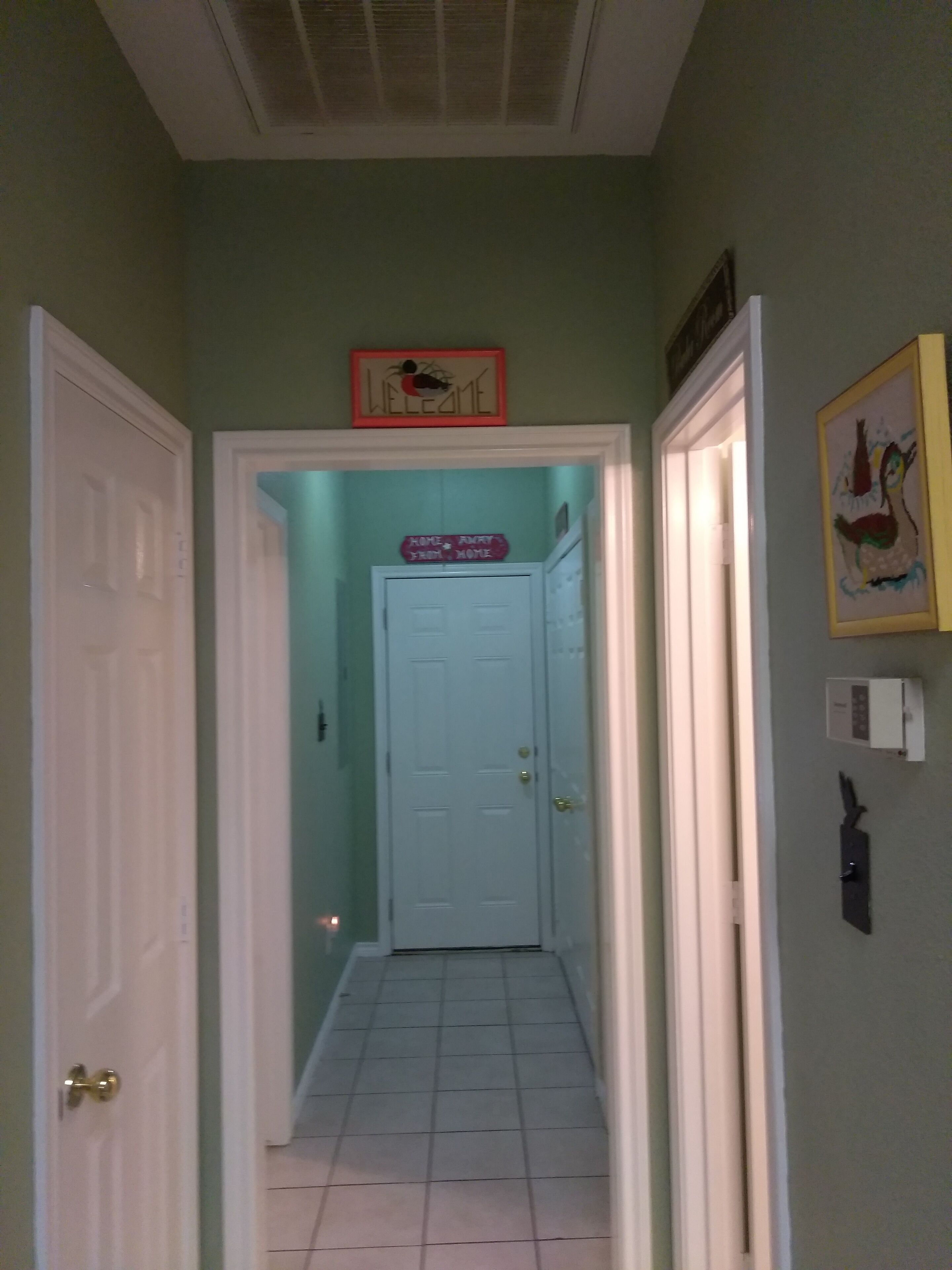 A hallway with a light blue door at the end, a welcome sign above it, and a framed picture on the wall.