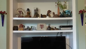 Ein an der Wand befestigtes Fernsehgerät der Marke Samsung, über einem weißen Unterhaltungsschrank mit Regalen für diverse Gegenstände.