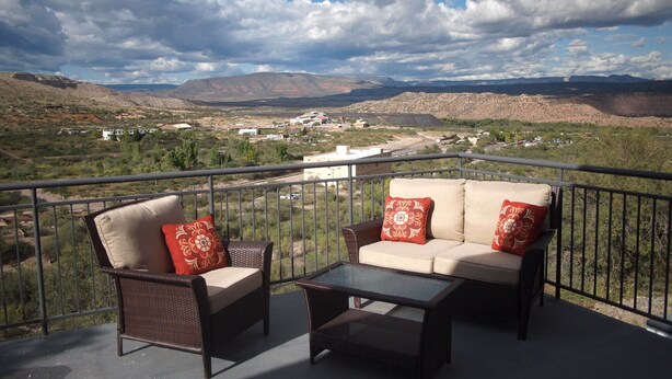 A balcony with wicker furniture and a glass table, overlooking a valley with buildings and mountains. - The Historic Clarkdale Lodge is your adventure headquarters! (Clarkdale)