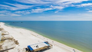 A beach with a pier extending into the water, a lifeguard station, and clear skies. - Seawind 1505 | Updated condo with perfect beach view and walk to dine, shop, more! (Gulf Shores)