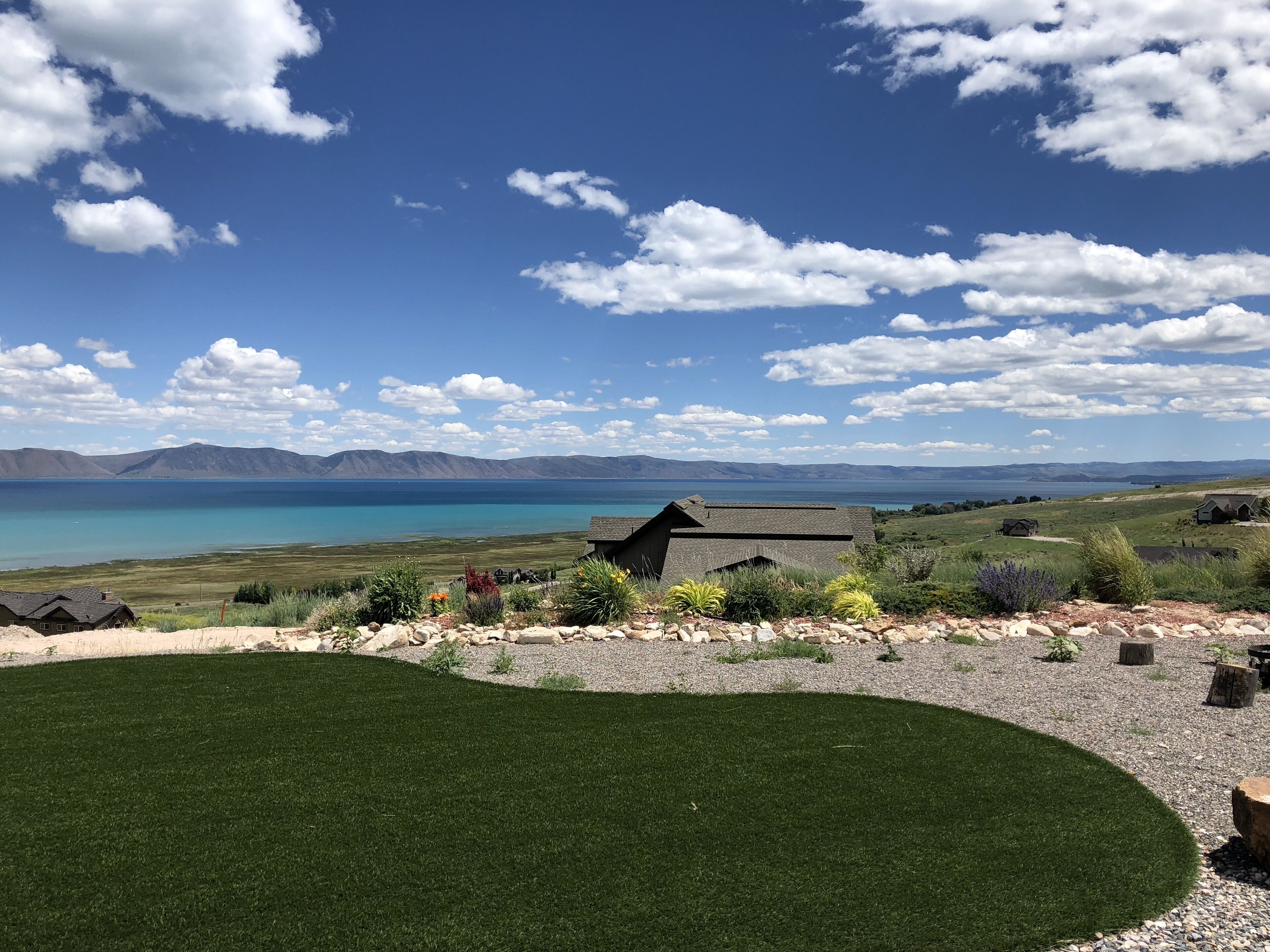 Une vue pittoresque d’une propriété au bord du lac, avec une pelouse verdoyante, un petit bâtiment et des montagnes à l’horizon.