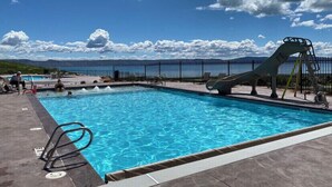 Una piscina con tobogán, sillas de descanso y vistas al mar y a las montañas.