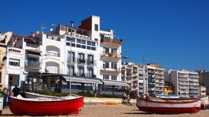 Un hotel frente a la playa con varios balcones, un área de estar cubierta y varios barcos en la arena.