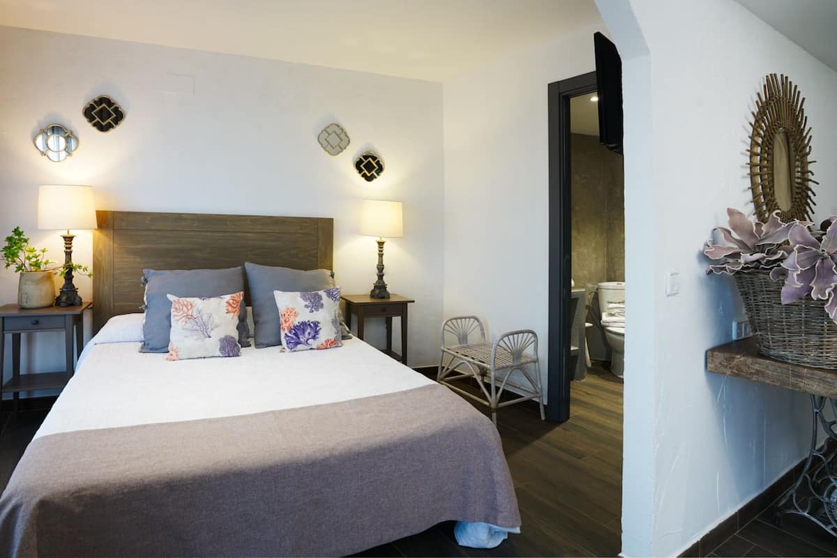Un dormitorio con una cama grande, dos mesitas de noche con lámparas, una silla y un espejo decorativo en la pared.