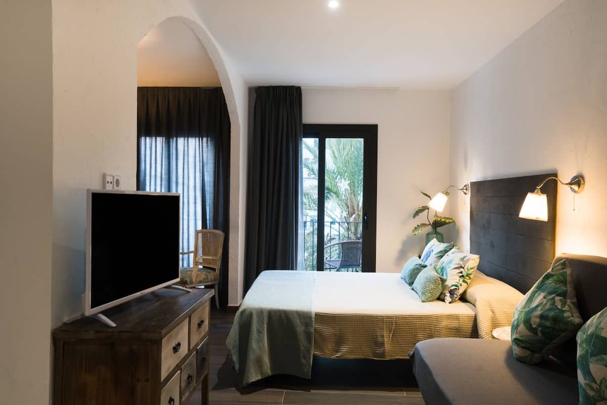 Un dormitorio moderno con cama, sofá, televisión y balcón con cortinas.