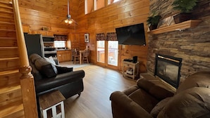 A cozy cabin interior with a wooden interior, a stone fireplace, a flat-screen TV, and a dining area. - 7 minutes to Parkway, hot tub, WiFi , pet friendly (Sevier County)