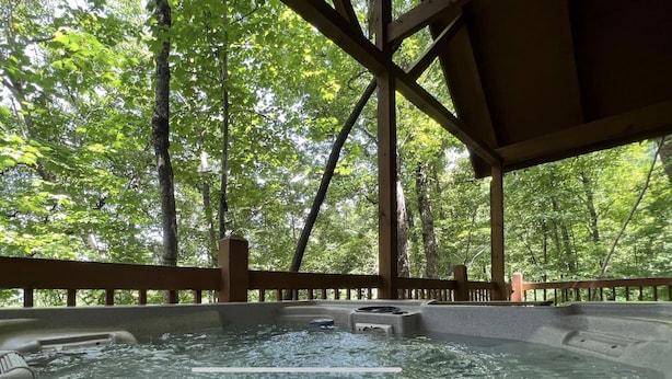A hot tub with a wooden deck and railings, surrounded by a forested area. - 7 minutes to Parkway, hot tub, WiFi , pet friendly (Sevier County)