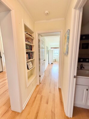 Un couloir avec une bibliothèque, une porte donnant sur une salle de bain et une vue sur une autre pièce.