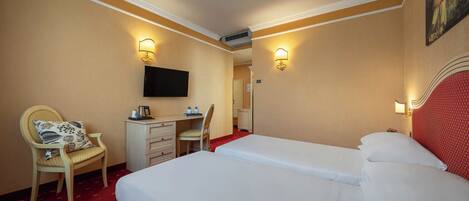 A hotel room with two beds, a desk, a chair, and a television on the wall.