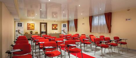 Un salón de conferencias con sillas y alfombra rojas, una mesa de recepción y obras de arte en las paredes.