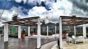 A covered outdoor area with a wooden deck, white pillars, and seating arrangements. - Cartoonstay Minion 01 Midhills Genting (Genting Highlands)