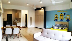 A modern living room with a sofa and a dining area with chairs and a table. There is a kitchen area with cabinets and a ceiling fan. - Cartoonstay Minion 01 Midhills Genting (Genting Highlands)
