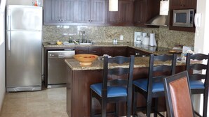 A kitchen with dark wooden cabinets, a stainless steel refrigerator, a granite countertop, and a built-in microwave. There are four wooden chairs with blue cushions. -  Montecristo Luxury Villa#11-Christmas/New Years-Highest Pt/Best View-12/16-1/17 (Quivira)