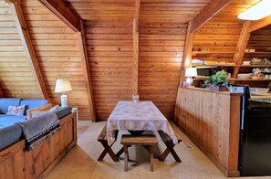 A cozy cabin interior with a wooden dining table, bench, and a sofa with a lamp.
