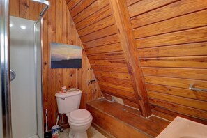 A wooden-paneled bathroom with a toilet, a sink, and a shower area.