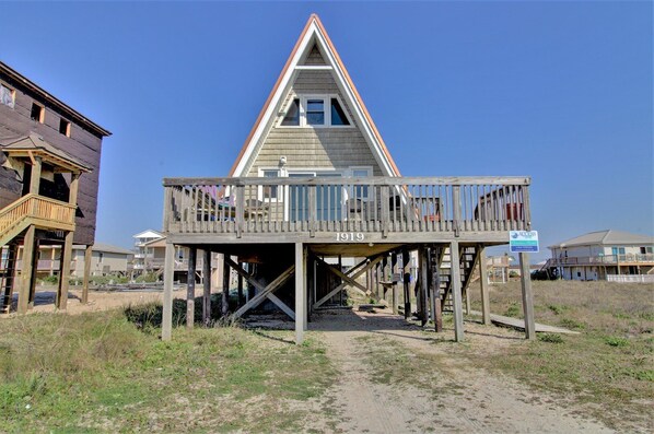 A wooden beach house with a balcony, a number '1919' on the front, and a sign indicating 'Access to Top of Beach'.