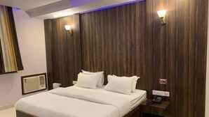 A hotel room with a large bed, a bedside table with a phone, and a wall-mounted light fixture. - The Ravindram (Rewari)