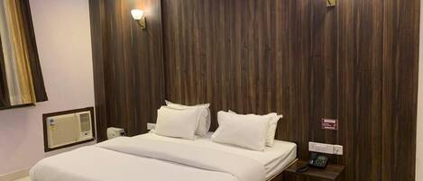 Quarto de hotel com uma cama grande, uma mesa de cabeceira com telefone e luminária na parede.