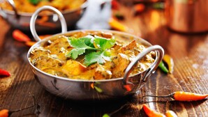 A bowl of curry with a garnish of cilantro, placed on a wooden surface with scattered chili peppers. - The Ravindram (Rewari)