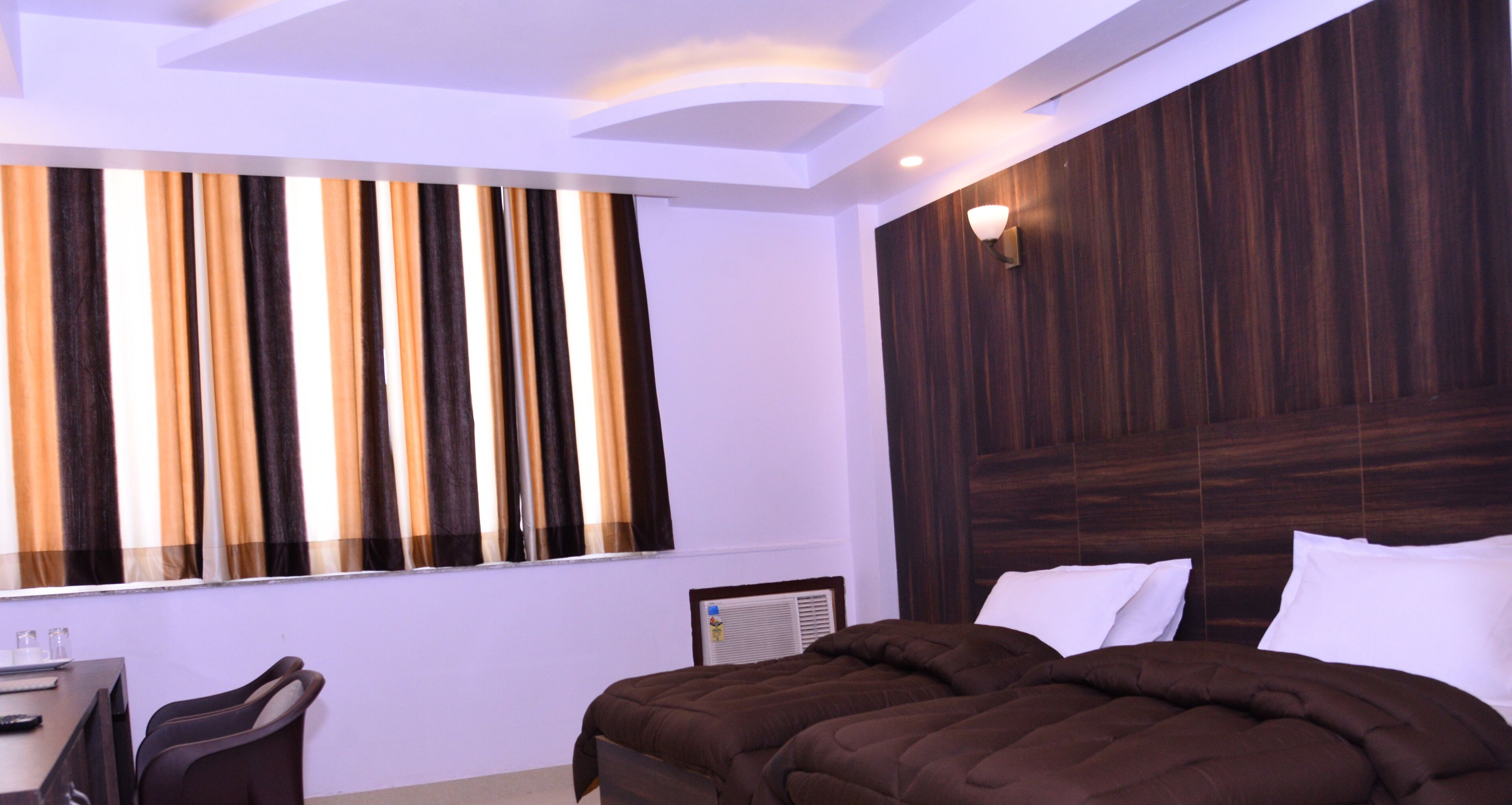 Una habitación de hotel moderna con una cama grande, un escritorio con una silla y un ventanal con cortinas a rayas.