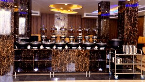 A modern kitchen area with marble countertops, multiple coffee machines, and a cart with kitchenware. - The Ravindram (Rewari)