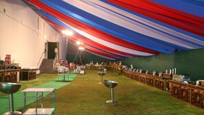 A banquet hall with a green carpet, tables with metal bowls, and a staircase leading to a higher level. - The Ravindram (Rewari)