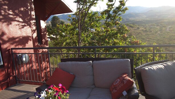 Un balcon avec un canapé en osier, une plante en pot et une vue sur un paysage montagneux.