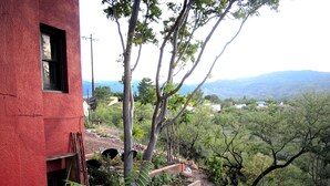 Un bâtiment rouge avec une fenêtre, entouré d’arbres et offrant une vue sur des collines lointaines.