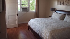 Une chambre à coucher avec un lit, une fenêtre avec des rideaux, un climatiseur fixé au mur et une table de chevet avec une lampe.