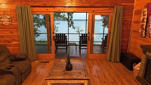 L’intérieur d’un chalet accueillant, avec un plancher en bois, un canapé, une table basse agrémentée d’une plante, et une vue sur un lac, visible à travers de grandes portes vitrées.