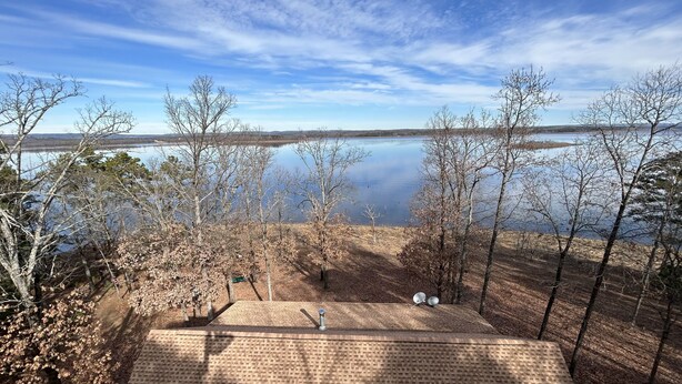 Une vue d’un lac sous un ciel dégagé, entouré d’arbres, avec une construction en briques au premier plan.