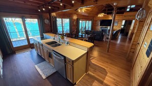 A spacious kitchen with a large island, wooden flooring, and a view of the outdoors through large windows.