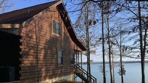 A wooden cabin with a porch and a staircase leading to a deck overlooking a lake.