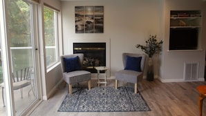 A living room with a fireplace, two armchairs, a rug, and a large window.