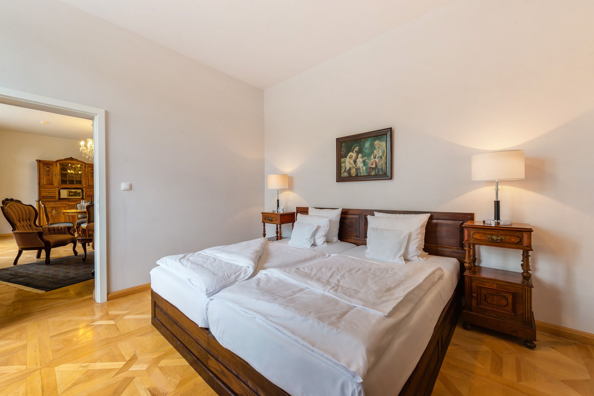 A hotel room with a large bed, two bedside tables with lamps, a wooden dresser, and a painting on the wall.