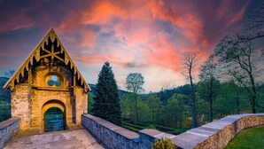 A stone building with a pointed roof and a circular window, surrounded by trees and a stone pathway. - Schlosshotel Purschenstein (Neuhausen)